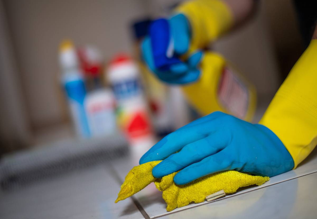 person wearing rubber gloves using yellow rag to clean tile