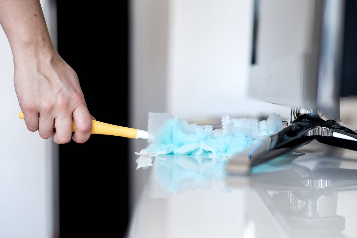 person using duster to clean white cabinet