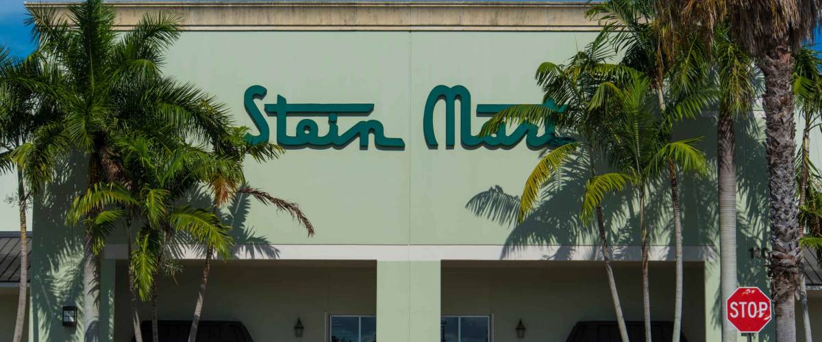 Palm Beach, FL USA 07/10/2019 Stein Mart South Florida Business Exterior with Sign Slightly Obscured By Tall Palm Trees